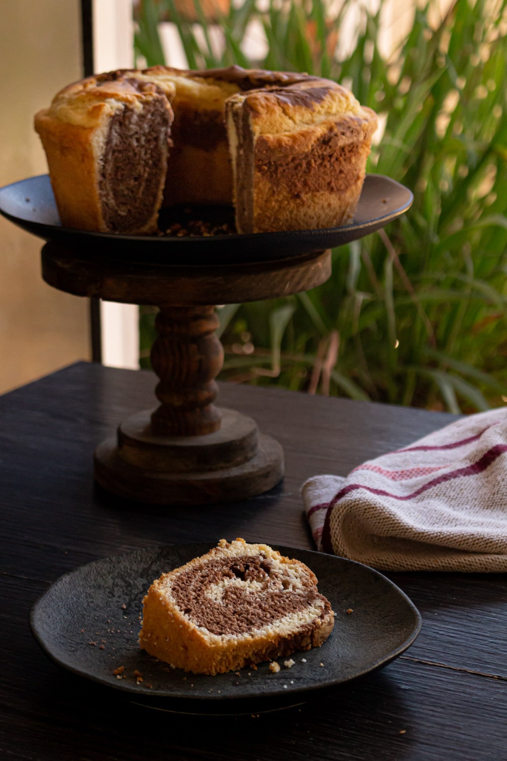 bolo mármore num prato alto de madeira e na mesa um prato com uma fatia do bolo