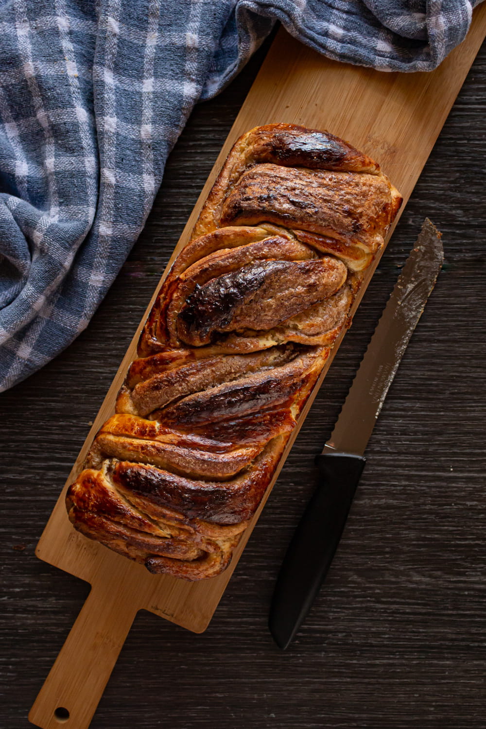 babka de canela vista de cima, sobre uma tábua de madeira e ao lado de um pano xadrez azul