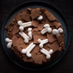 foto de cima do bolo de chocolate com o topo todo quebrado e ossinhos de suspiro por cima