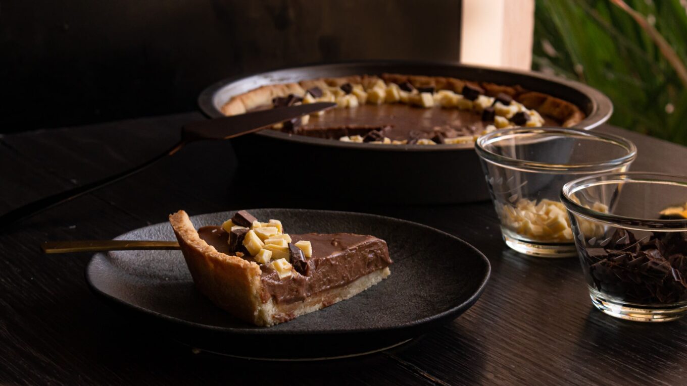 foto colorida de uma fatia da torta simples de chocolate e ao fundo a assadeira com o restante da torta