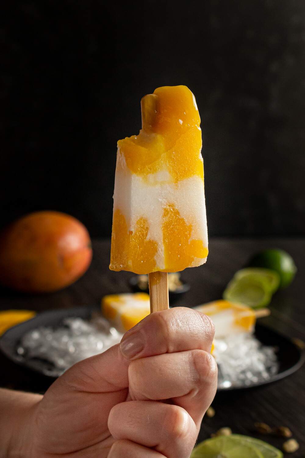 mão segurando um picolé de manga com coco já mordido