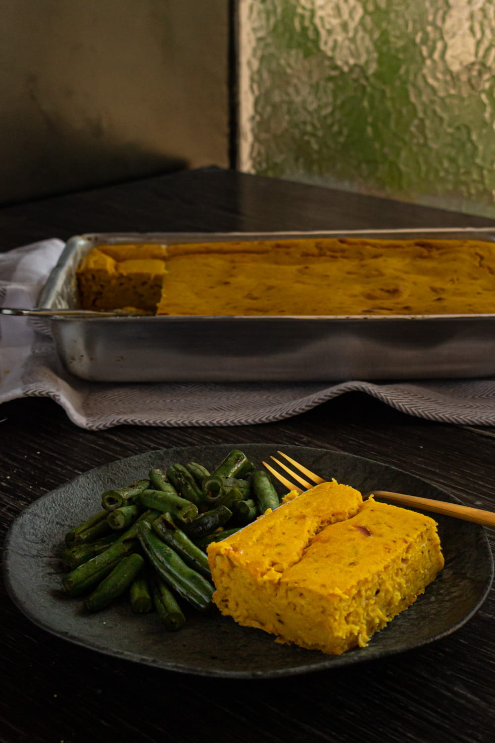 Foto lateral do prato com um pedaço de bolo salgado de abóbora e vagens salteadas