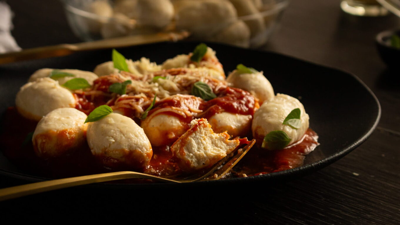 prato de gnudi com molho de tomate. Descansando no prato tem um garfo dourado segurando um gnudi já partido