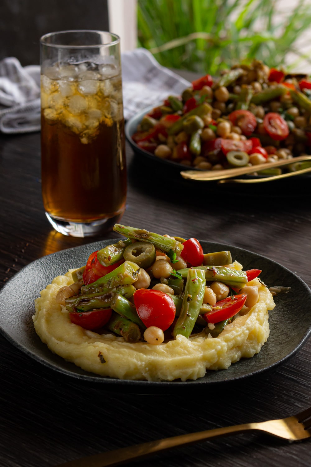 prato com purê de batata e salada de vagem por cima, atrás um copo de chá com pedras de gelo